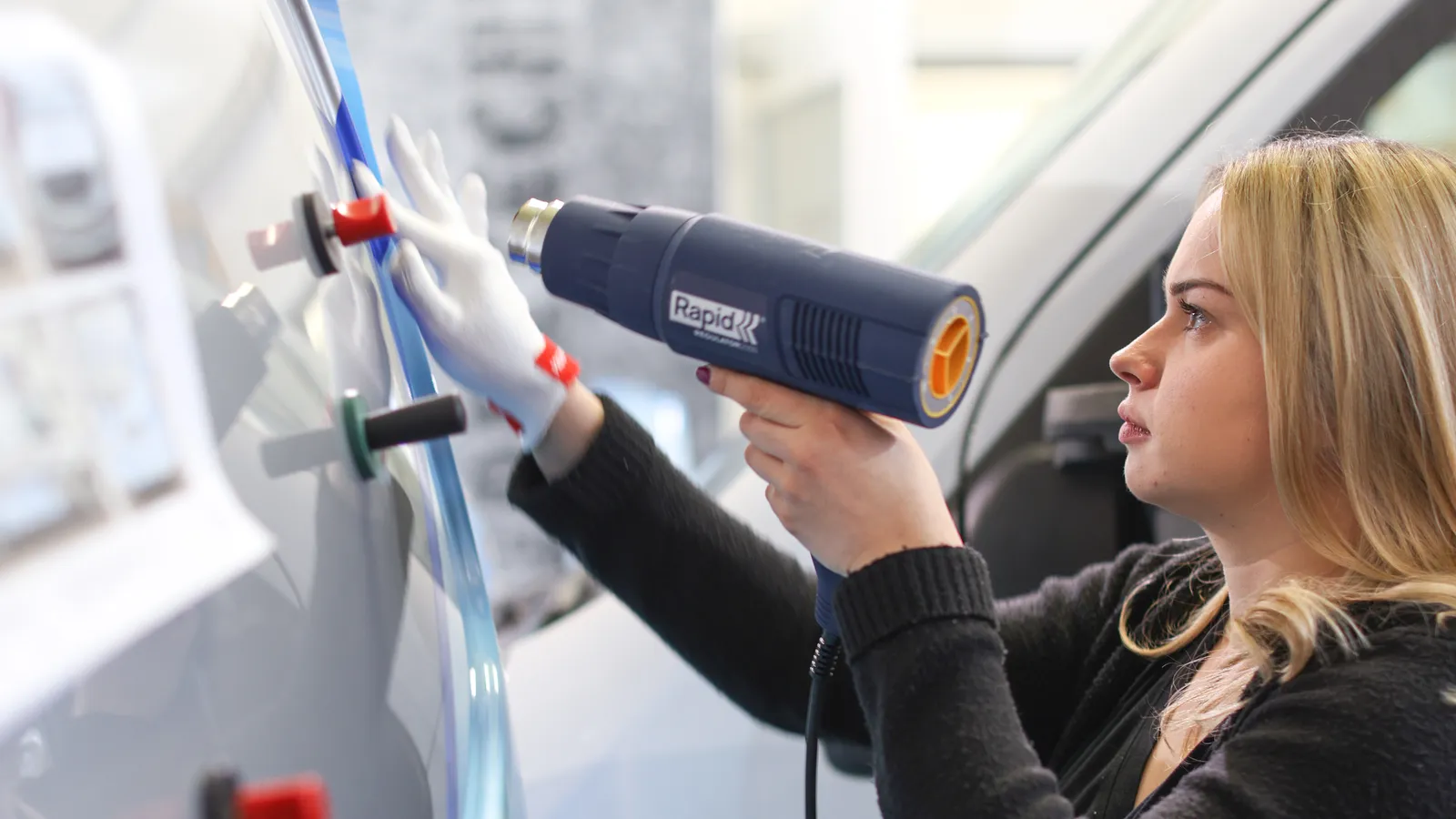 Mitarbeiterin von Fauss bringt mit dem Heißluftföhn eine Folie an einem Fahrzeug an